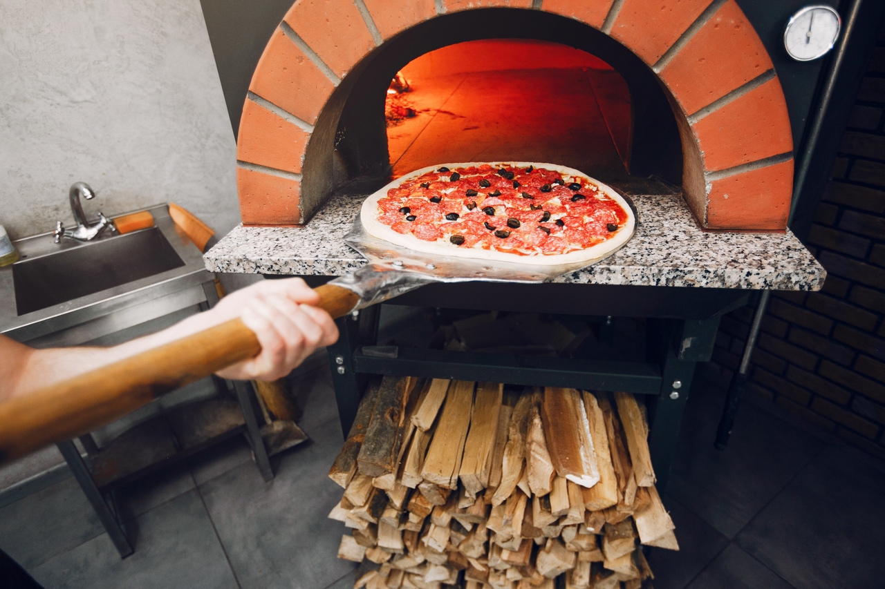 A person putting pizza into a wood fire oven