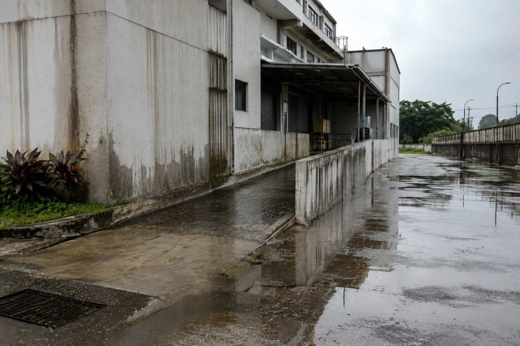 Rainwater pooling around an industrial building with stained walls and drainage issues