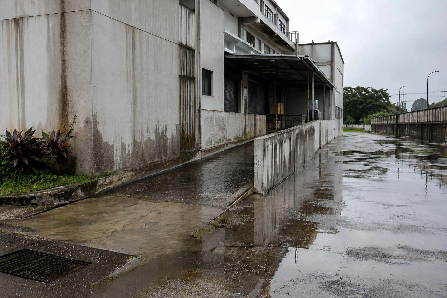 Rainwater pooling around an industrial building with stained walls and drainage issues