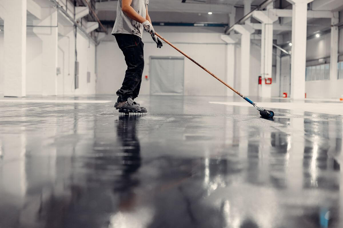 Worker applying epoxy flooring to create a smooth, seamless industrial floor surface