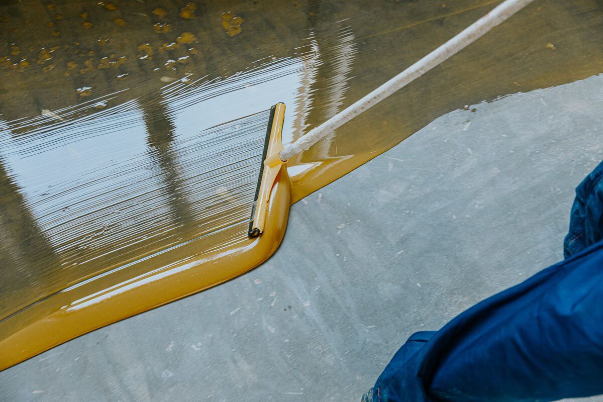 Worker applying liquid flooring material with a squeegee over a concrete surface