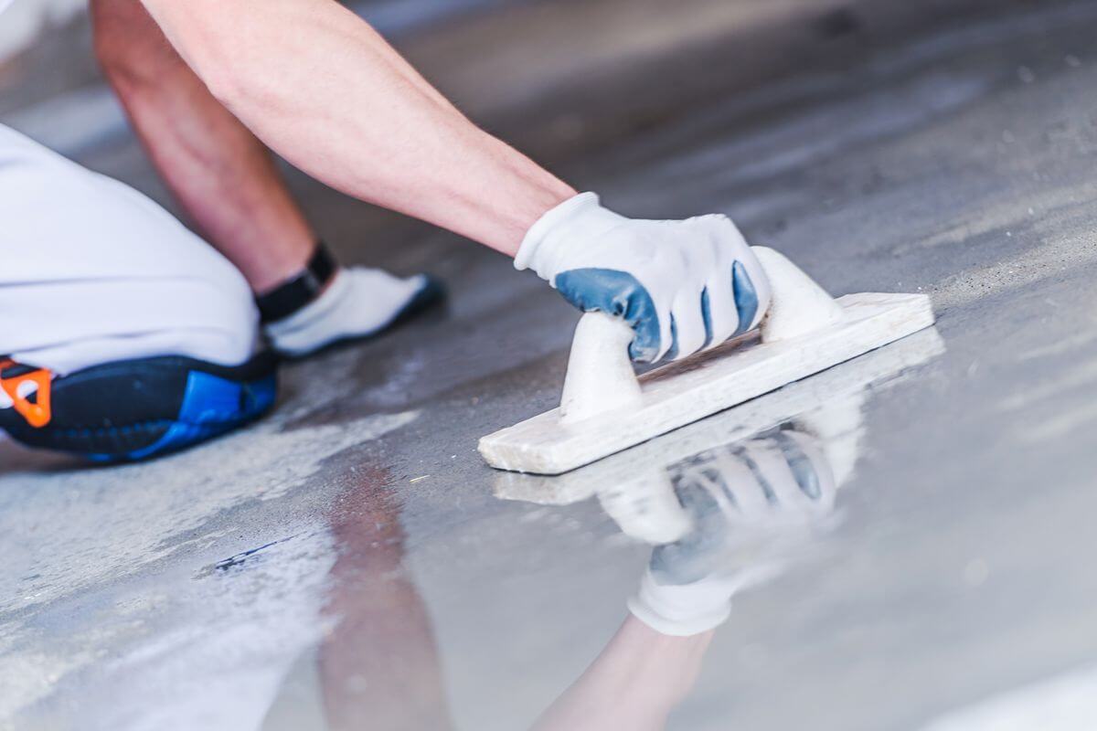 Flooring installer using a hand trowel to smooth a newly applied floor coating