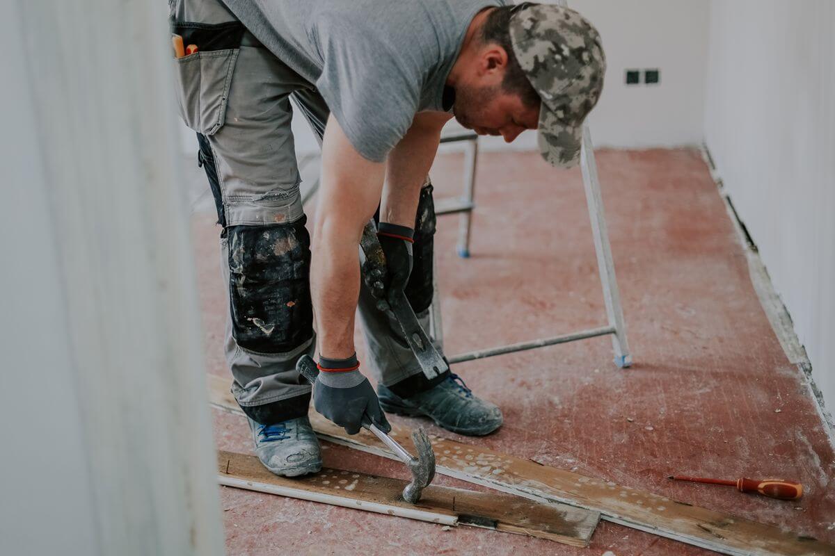 Flooring contractor using a hammer to remove old flooring during surface preparation