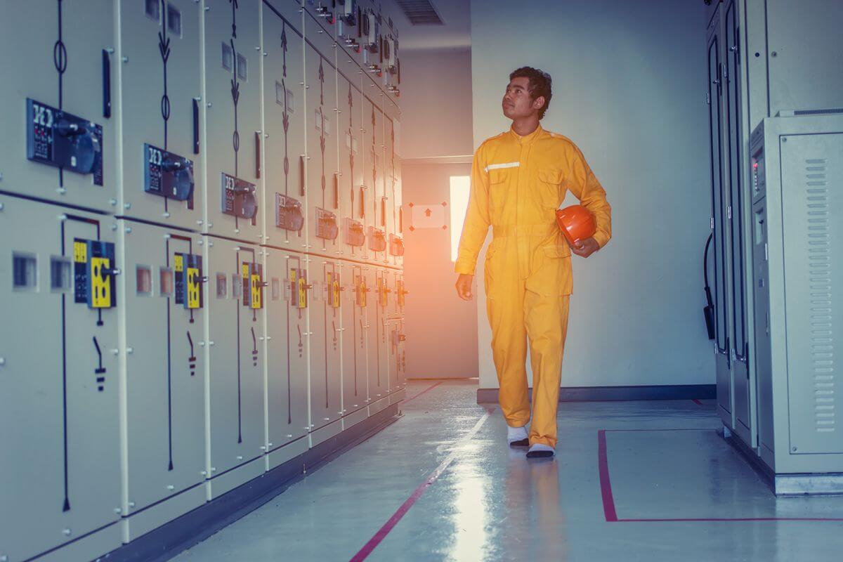 Worker wearing protective clothing walking through an electrical equipment room with smooth industrial flooring